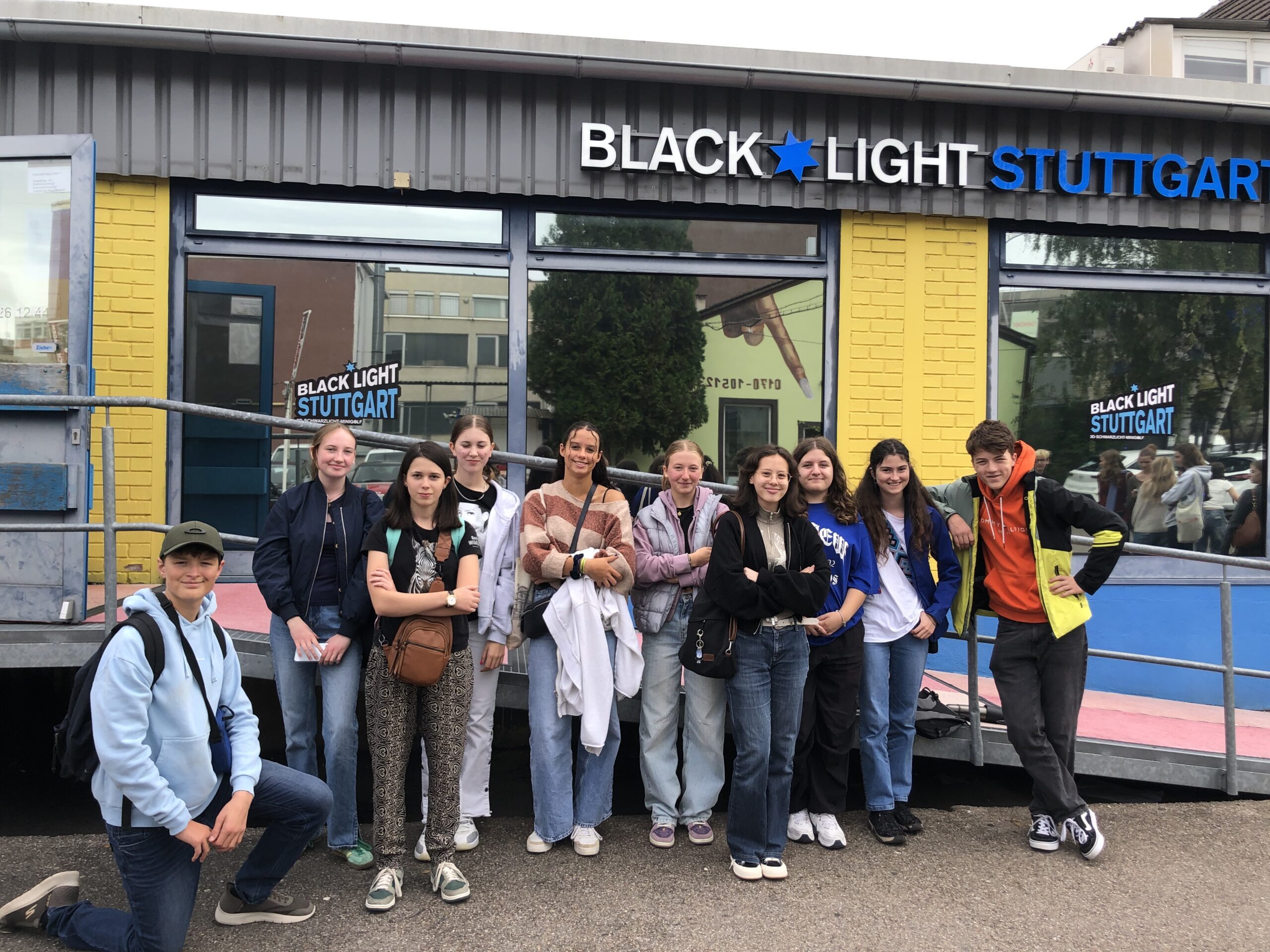 Gruppe Jugendlicher lächelnd, bunte Kleidung, vor einem Gebäude mit dem Schriftzug „Black Light“.