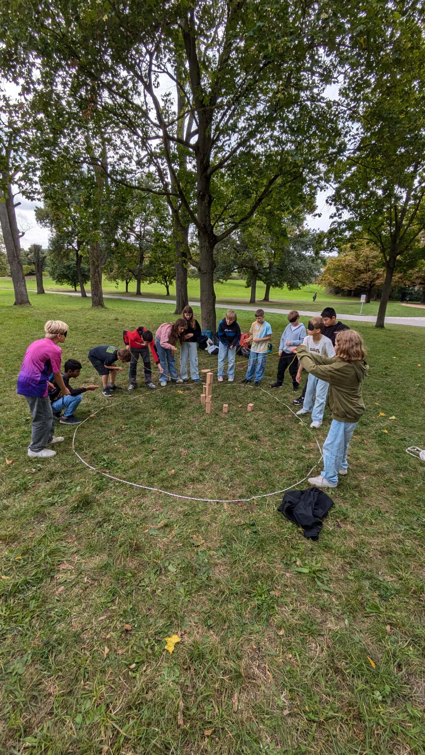 Eine Gruppe von Kindern spielt ein Wurfspiel im Park, umgeben von Bäumen, alle sind konzentriert.