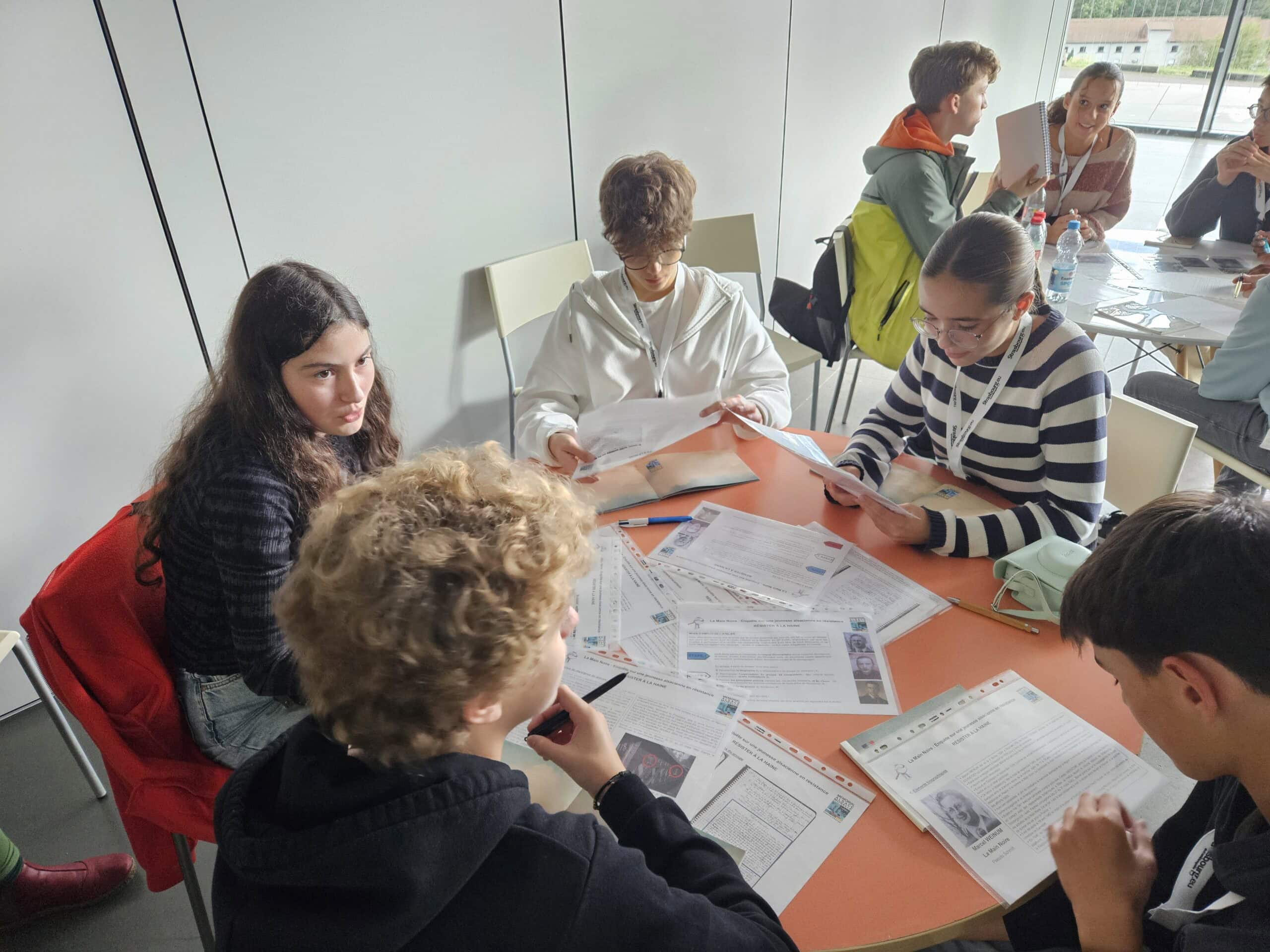 Junge Erwachsene diskutieren um einen Tisch, mit Dokumenten und Notizen, entspannt und aufmerksam.