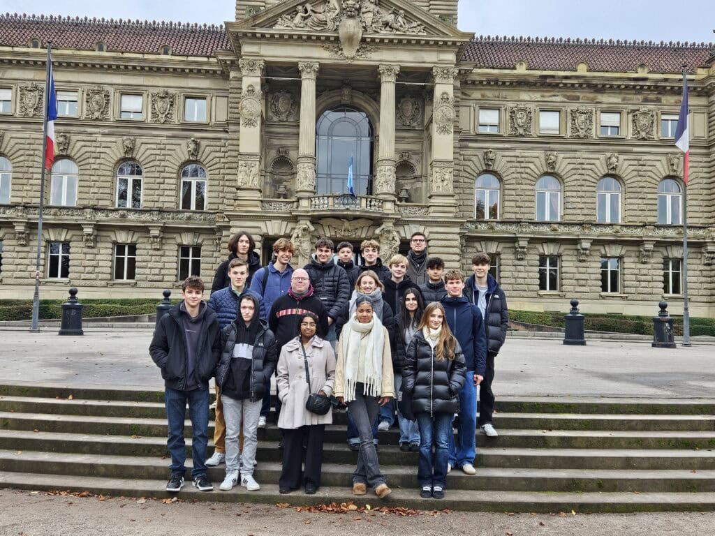 Gruppe von Menschen lächelt vor einem historischen Gebäude in Winterkleidung, beige und braun.