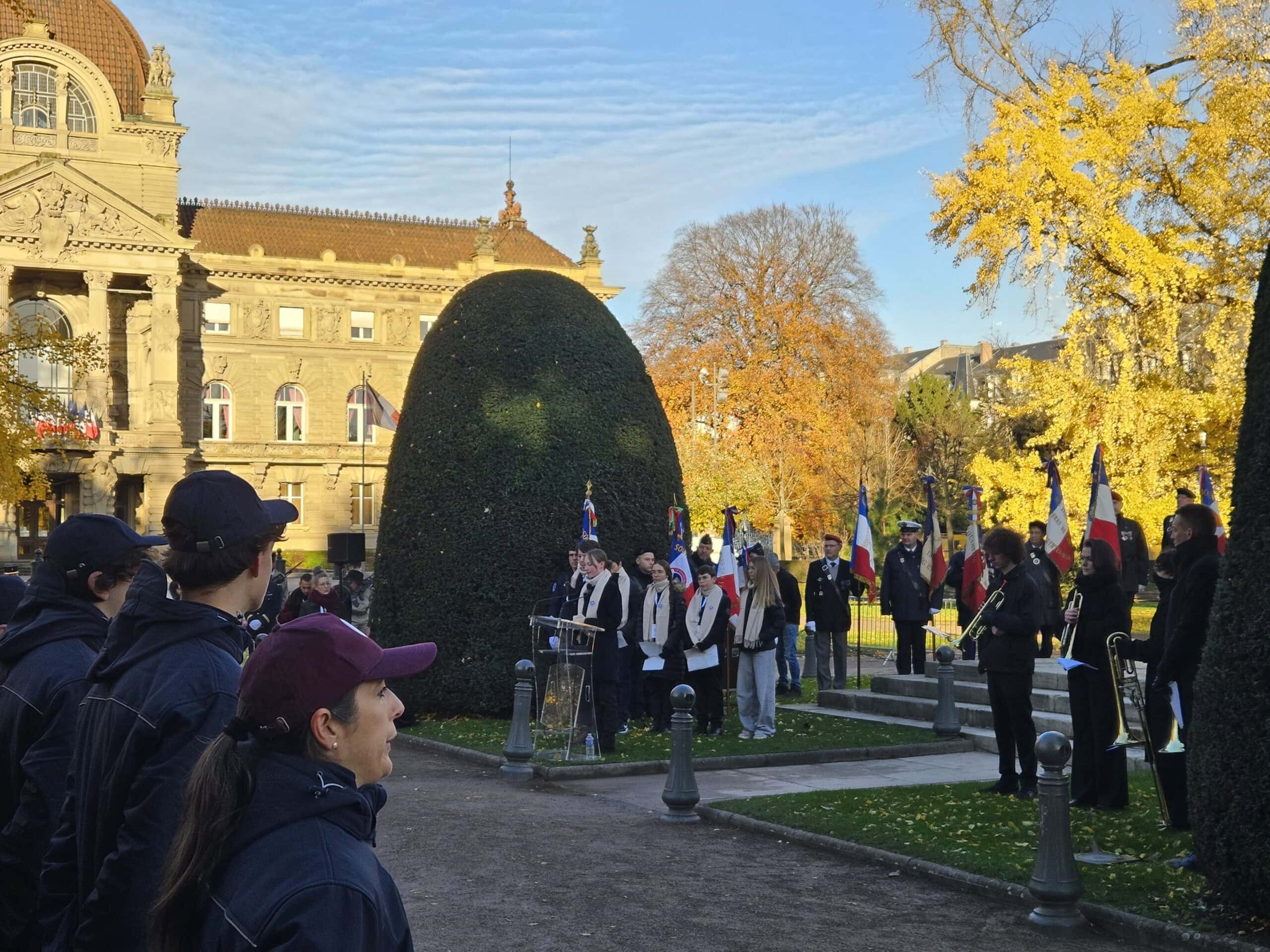 Eine Gruppe von Menschen steht bei einer Zeremonie in einem herbstlichen Park vor einem Gebäude.