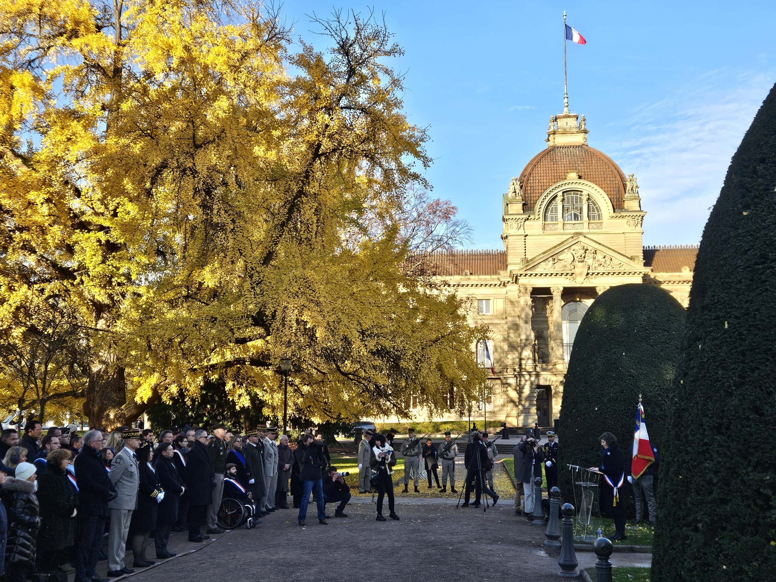 Versammlung von Menschen im Freien vor einem historischen Gebäude mit Herbstbäumen und Fotografen.