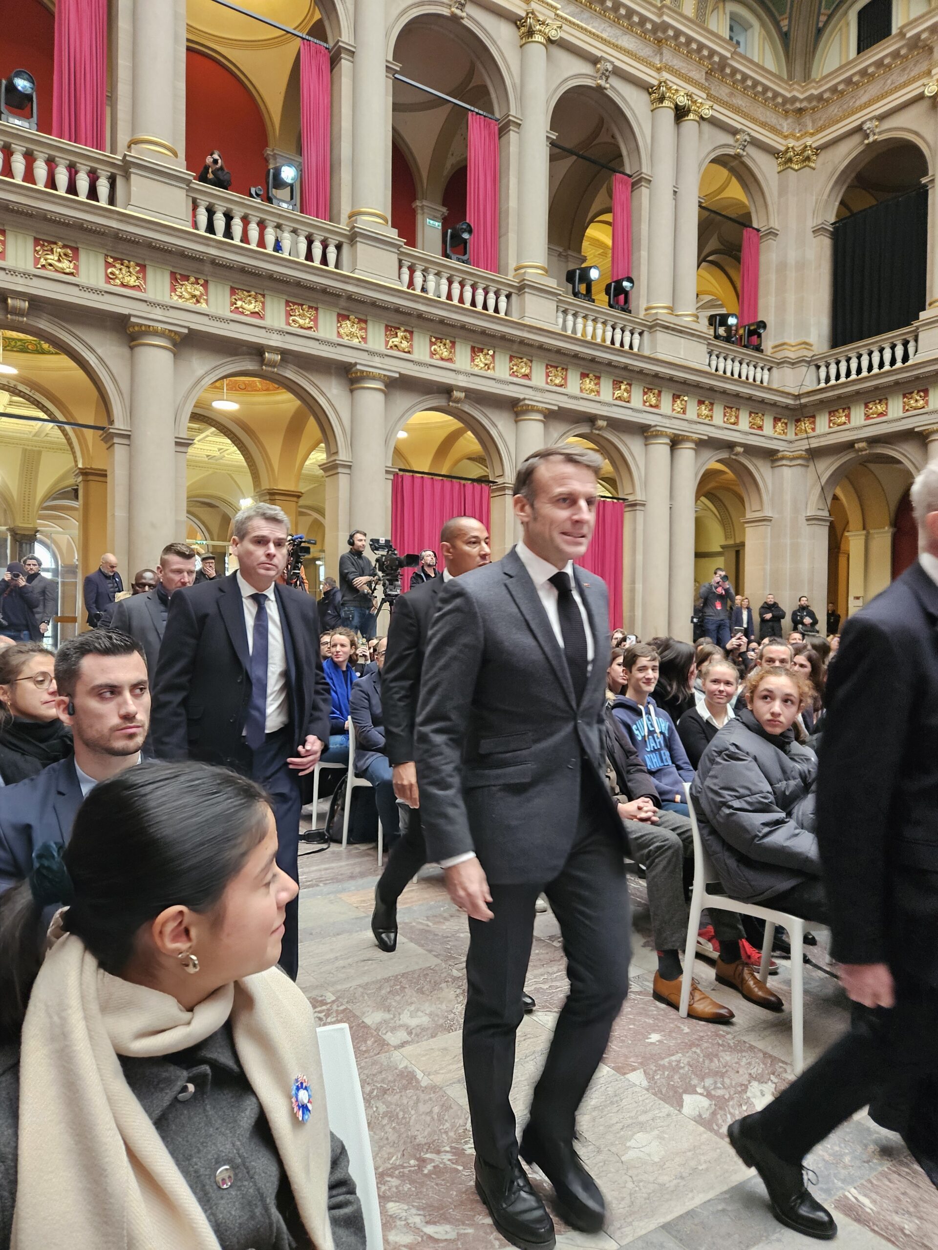 Eine elegant gekleidete Frau und Männer in Anzügen bei einer formellen Veranstaltung.