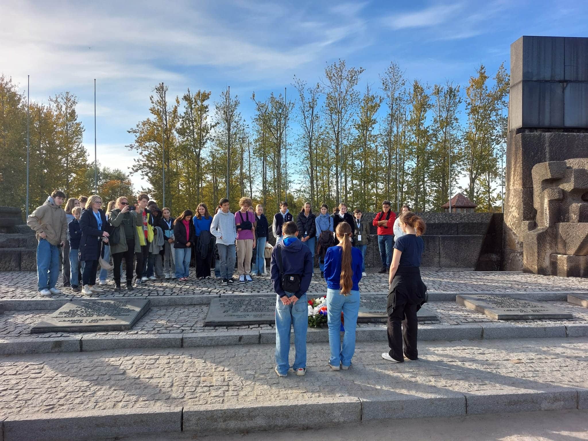 Eine Gruppe von Menschen steht draußen vor einem Denkmal, umgeben von Bäumen.