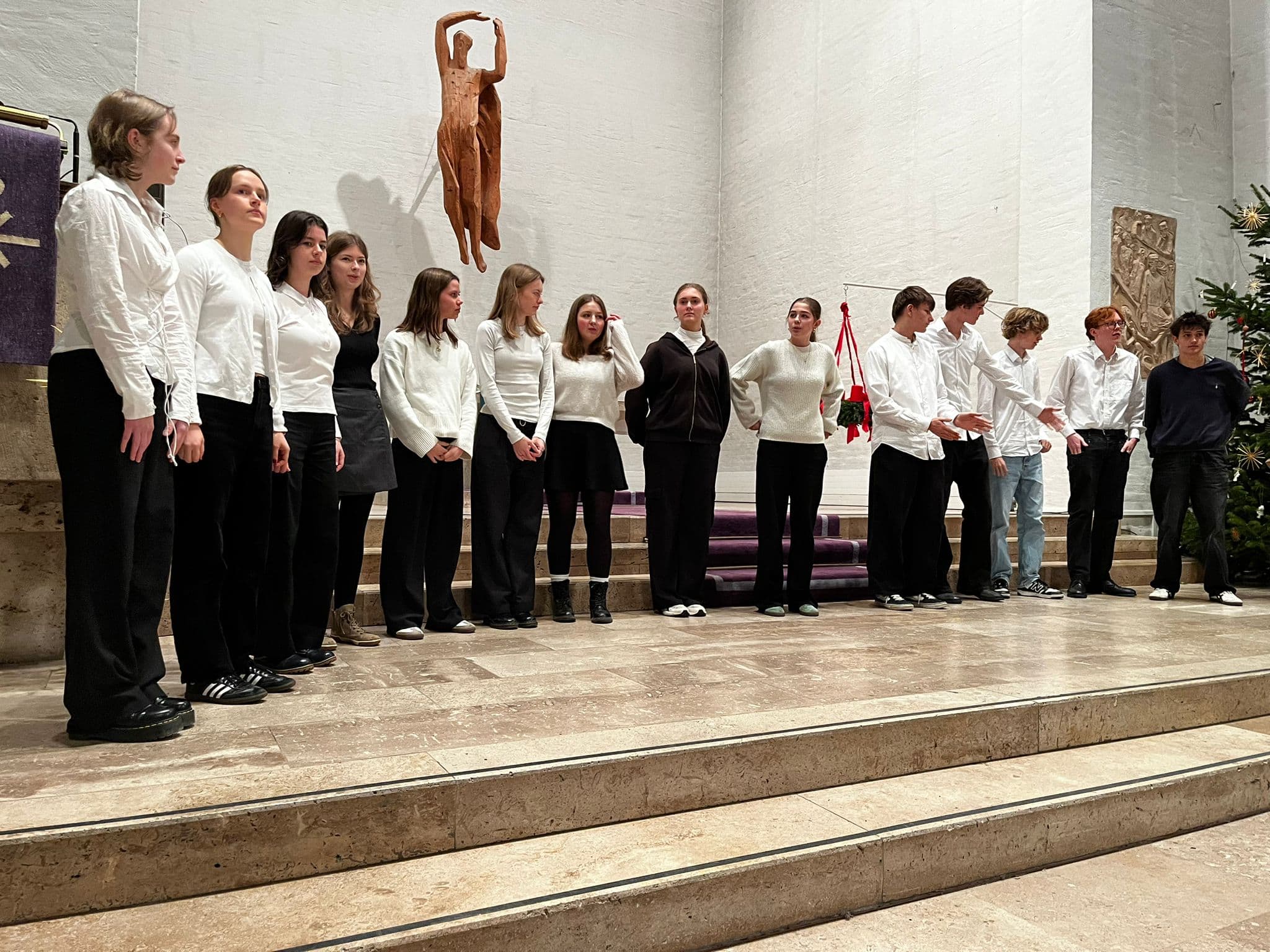 Eine Gruppe junger Menschen, lächelnd, in schwarzer und weißer Kleidung, steht auf Kirchenstufen.