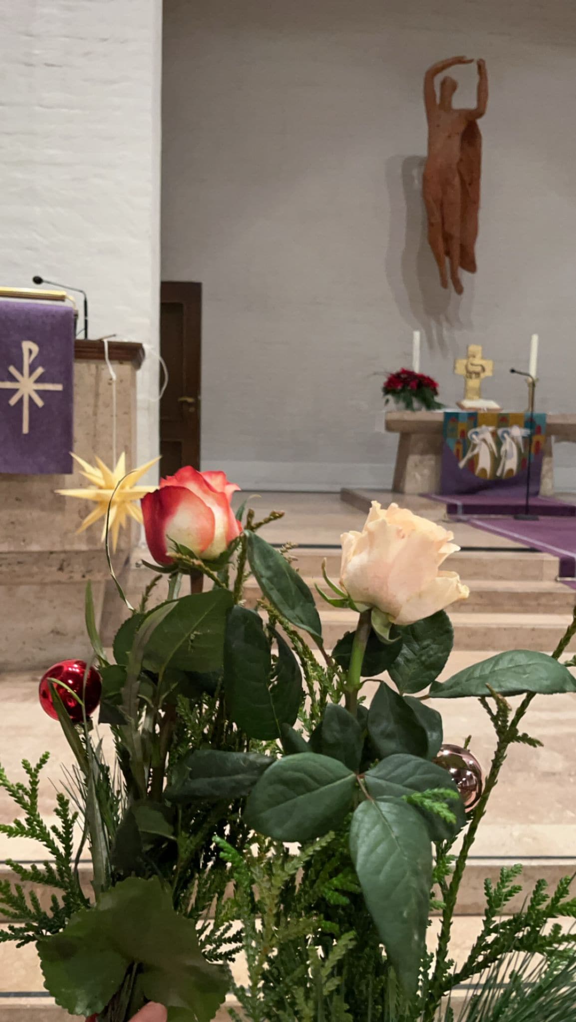 Blumenstrauß vor einem Altar mit Jesusstatue, rote und cremefarbene Rosen, festlich dekoriert.