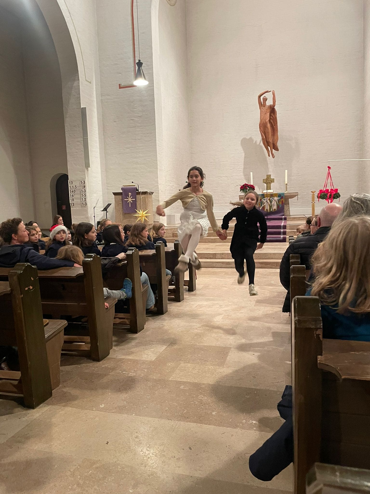 Zwei Kinder rennen lachend durch eine Kirche, geschmückt mit Adventsdekorationen.