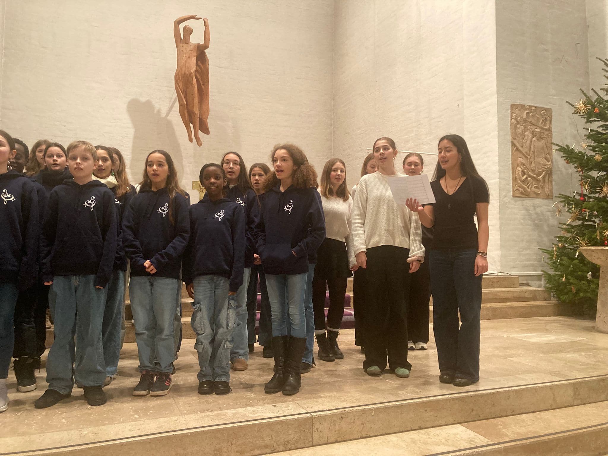 Eine Gruppe von jungen Menschen singt in einer Kirche mit feierlichen Ausdrücken, winterliche Kleidung.