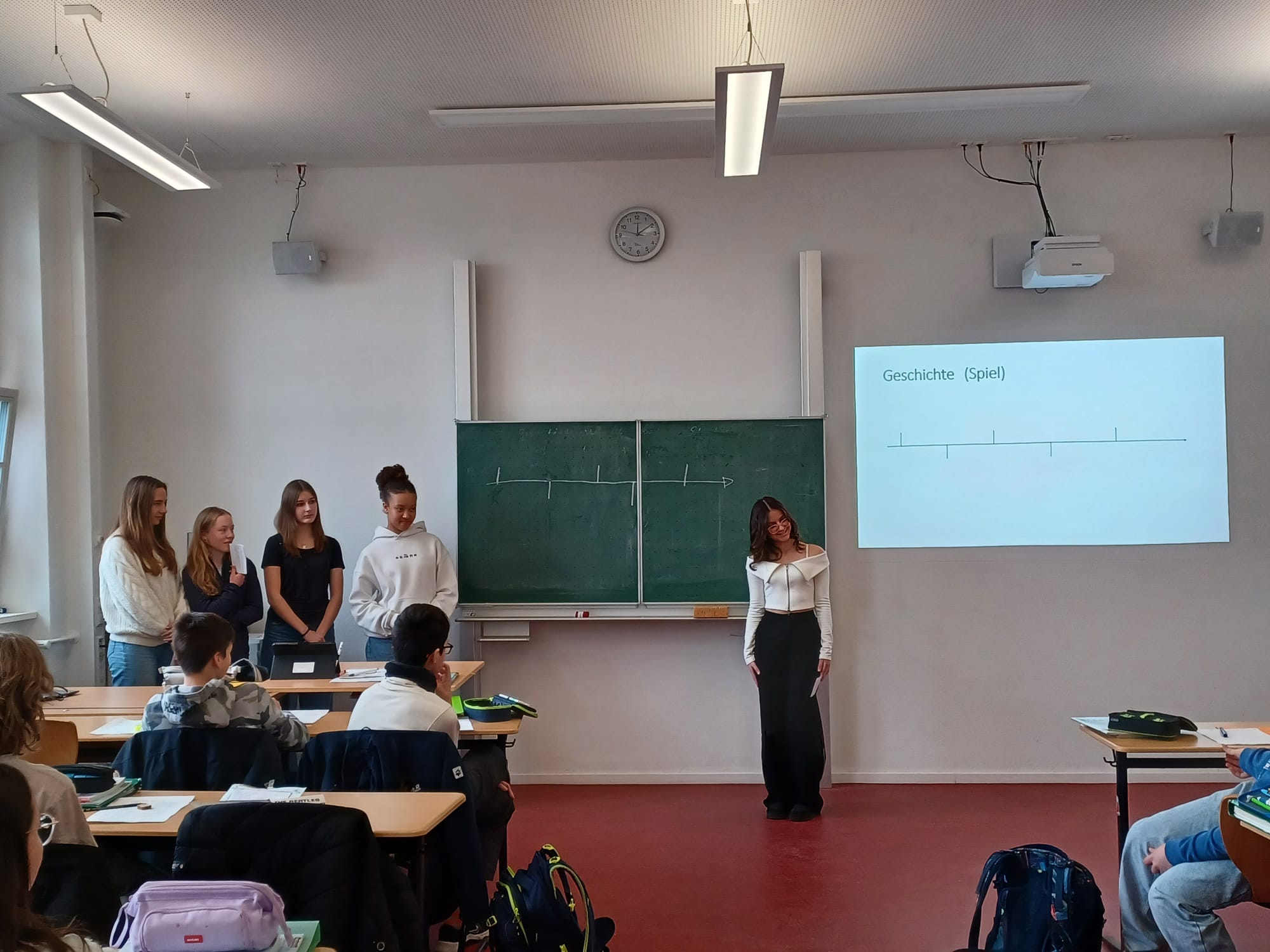 Eine Gruppe von fünf Schülern steht lächelnd vor einer Tafel in einem Klassenzimmer.