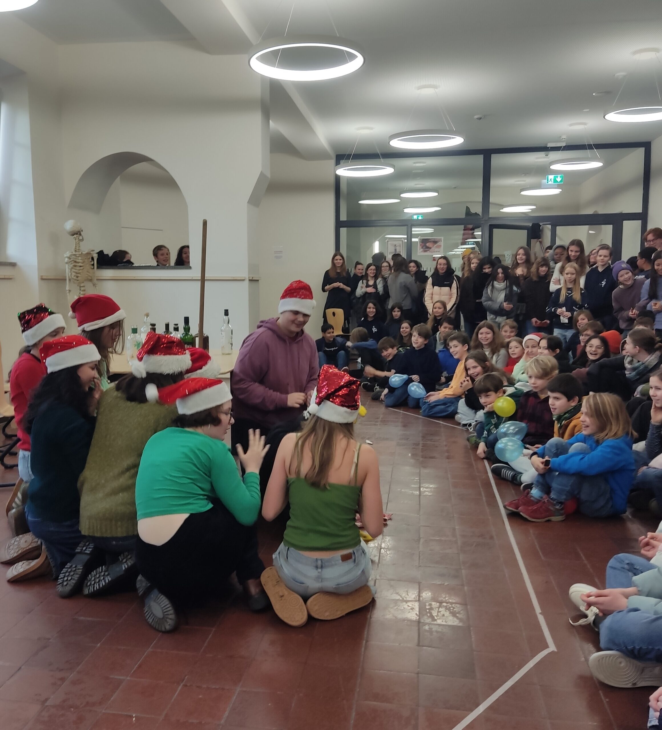 Gruppe fröhlich singender Menschen mit roten Mützen im festlich dekorierten Raum.