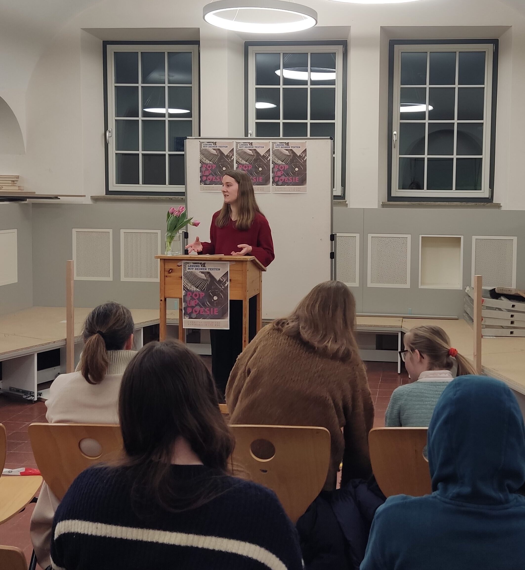 Eine Frau hält mit ernster Miene eine Präsentation vor Publikum in einem hellen Raum.